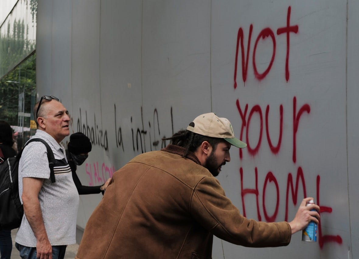 Protestor spray-painting "Not Your Home" on a wall during a demonstration against gentrification in Mexico City.