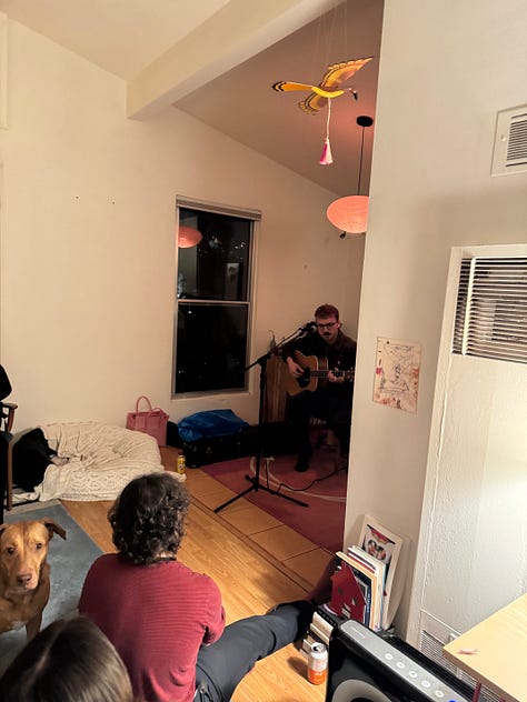 Photo 1: People gathering in a living room with vaulted ceilings. Photo 2: A painting and 3 drawings hung on a wall. Photo 3: A surrealist painting of amorphous creatures hanging from a tree. Photo 4: People gathered around the surrealist painting. Photo 5: A collage with cartoon images of a trail to the ocean and a butterfly, and bold text reading: traces of a path, losing sight of the sea. Photo 6: People and a red dog gathered around a man playing guitar. Photo 7: Ink and pastel drawings of two circles meeting. Photo 8: a pile of shoes at a door. Photo 9: Silhouettes of people through tall windows from outside at night.