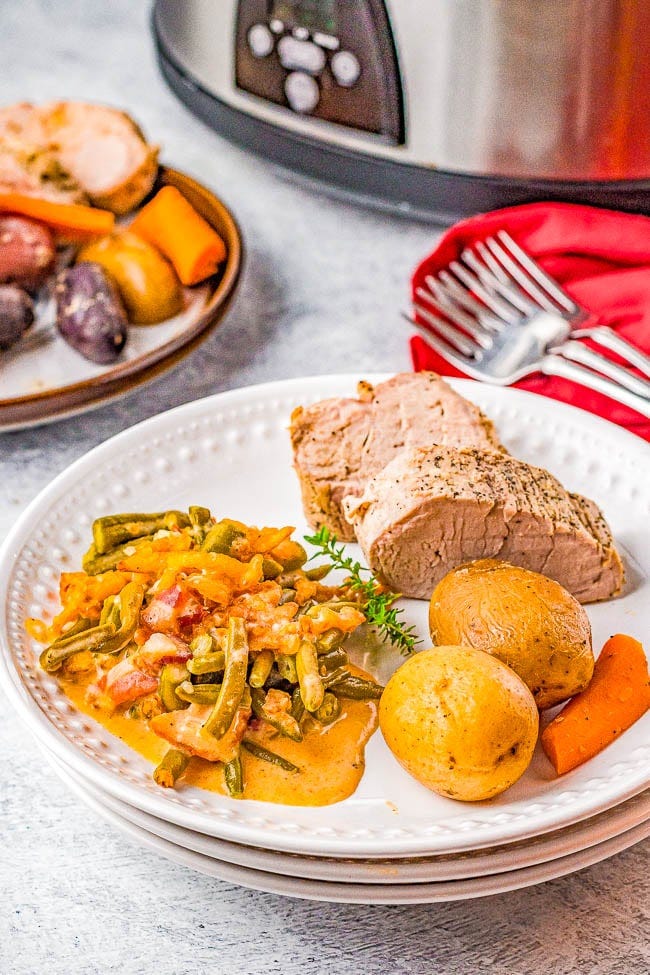 Cheesy Slow Cooker Green Bean Casserole on a plate with pork loin, potatoes, and carrots. 