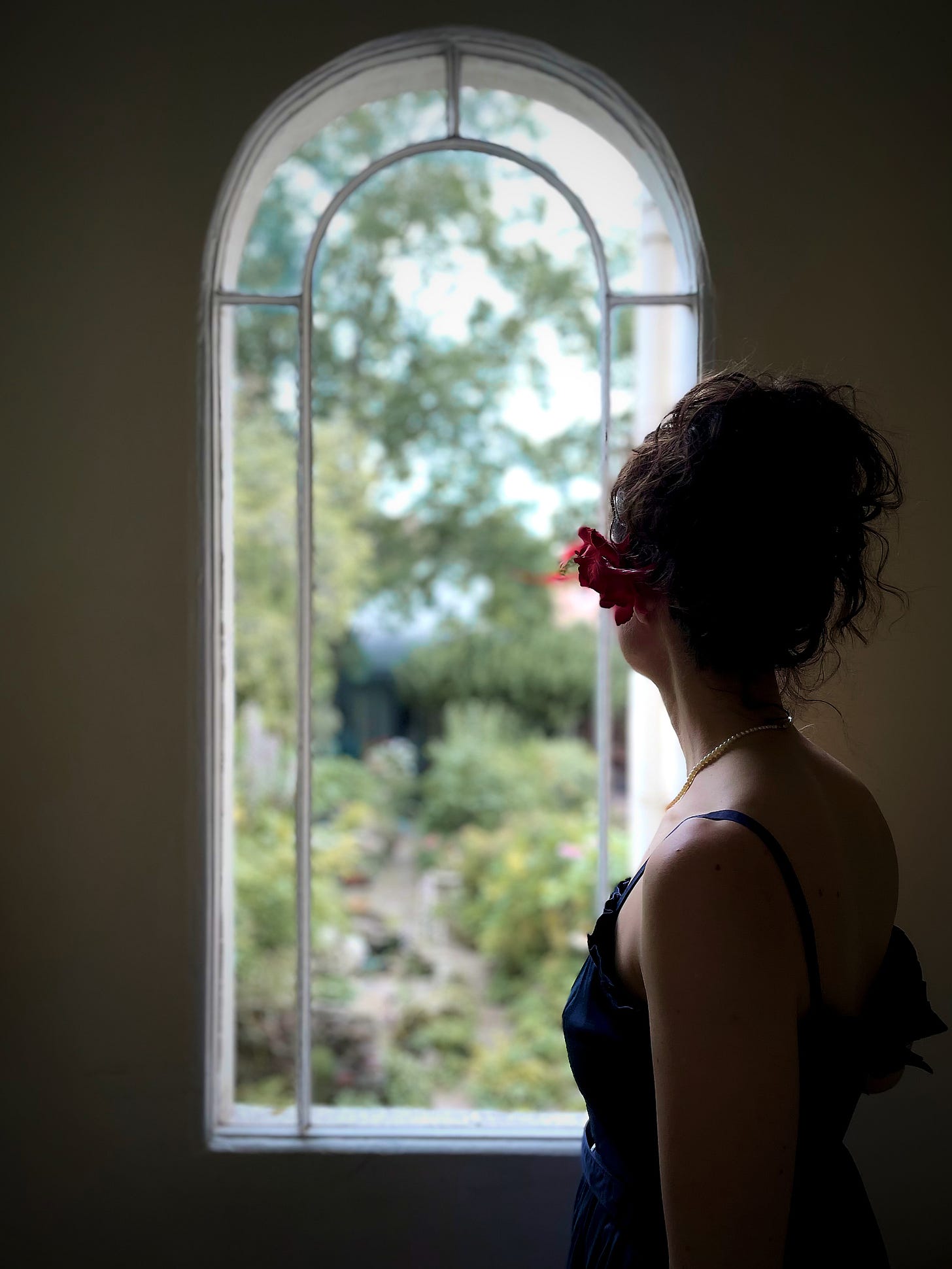 Danielle Styles looking out of a long window into a garden. Danielle Styles looking out of a long window into a garden.
