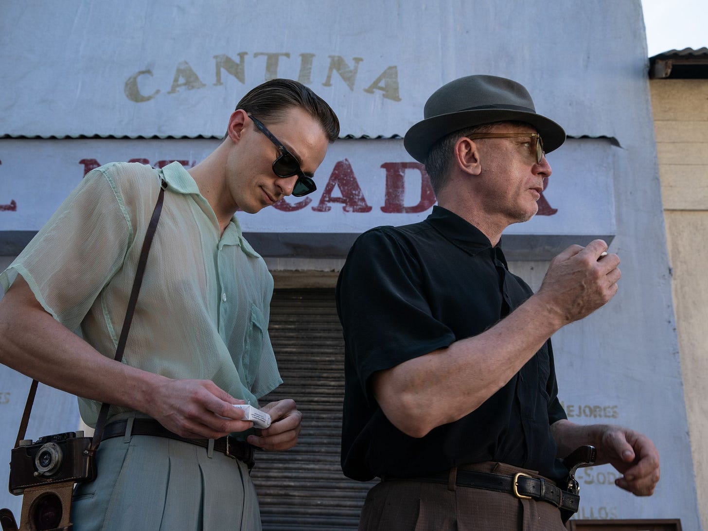 Drew Starkey and Daniel Craig smoke cigarettes outside a building that says "cantina" in "Queer" (2024)