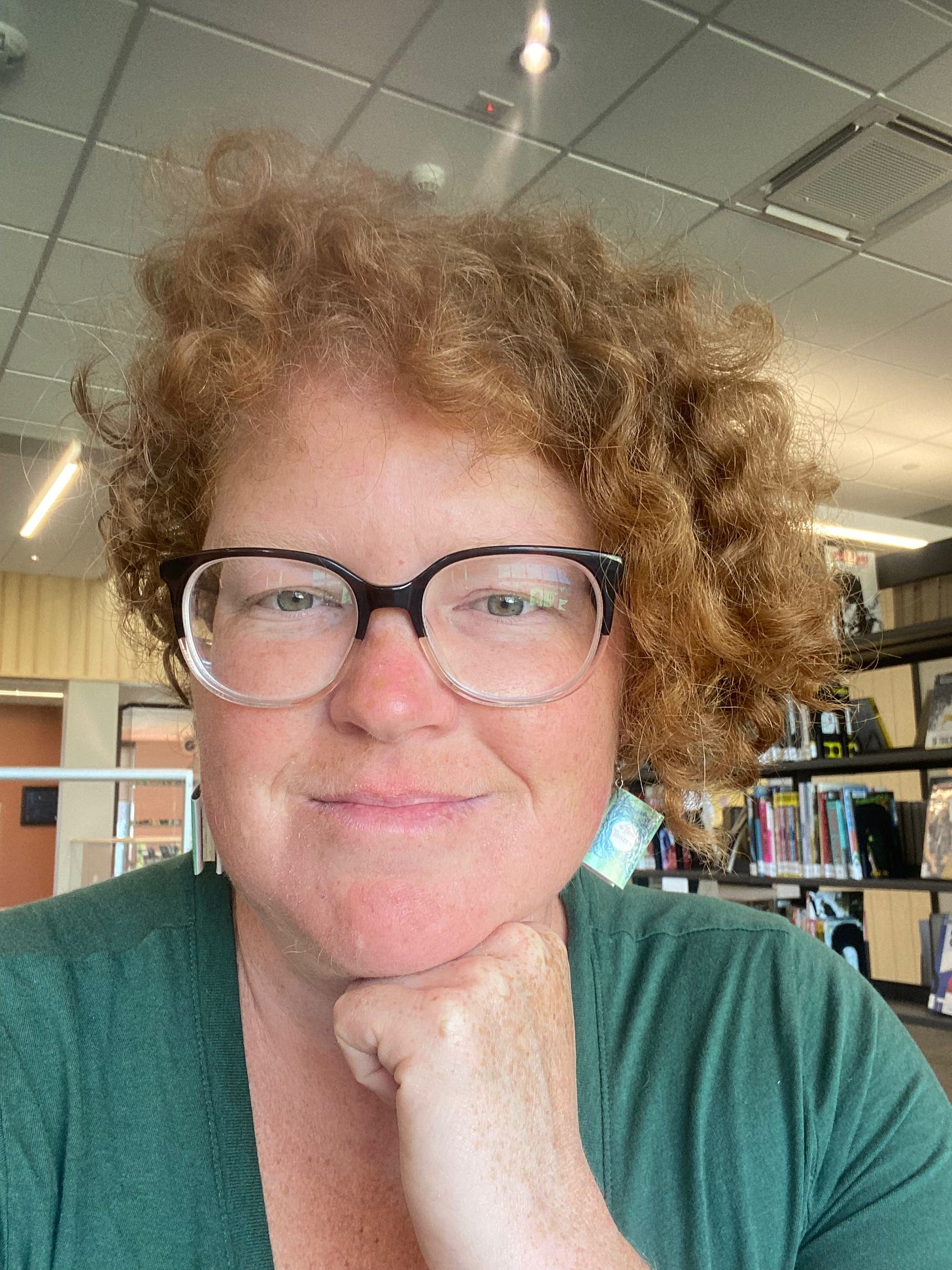 I’m sitting in the library in a green shirt. My earrings are tiny green books made of paper.