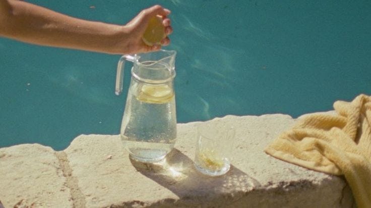 This may contain: a person is holding a lemon in a pitcher next to a pool with water and towels