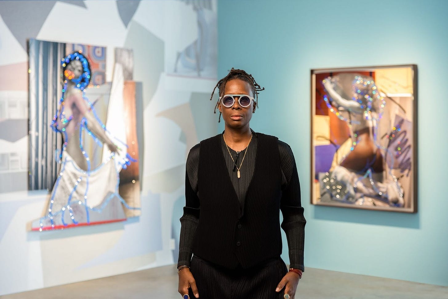 Portrait of Mickalene Thomas. Unfocused in the background are two of here pieces on either side of her.
