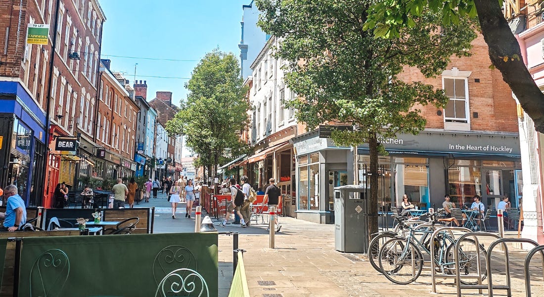 A street in Hockley in Nottingham with colourful buildings, people walking around, and a green seating area in front