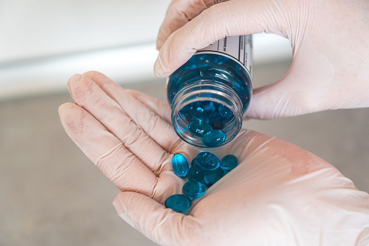 Photo by Castorly Stock on Pexels Close-up of a healthcare professional with latex gloves pouring blue capsules from a bottle. (stock photo)