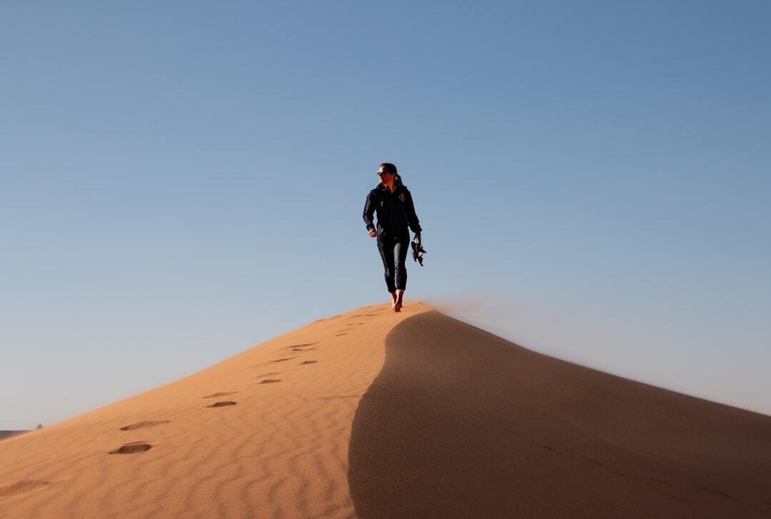 man in black jacket walking on brown sand during daytime man in black jacket walking on brown sand during daytime
