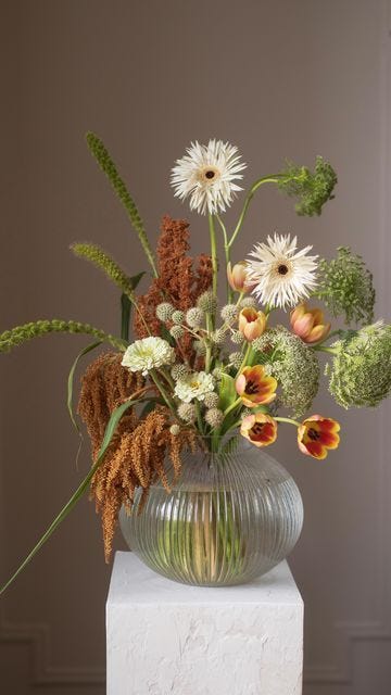 This may contain: a vase filled with lots of flowers on top of a white table next to a wall