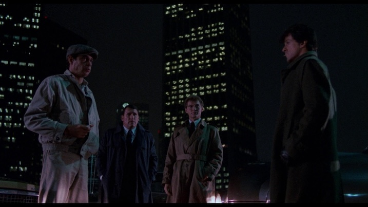 Rooftop scene from Cobra (1986) in 4K UHD – Stallone and fellow cast members meet at night in a city rooftop sequence, with skyscrapers in the Arrow restoration.