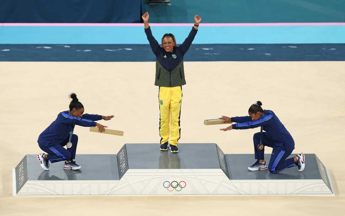 Gymnast Rebeca Andrade (center) of Brazil wins her first gold medal in Paris. Paying homage are silver medalist Simone Biles (left) and bronze medalist Jordan Chiles of the United States.
