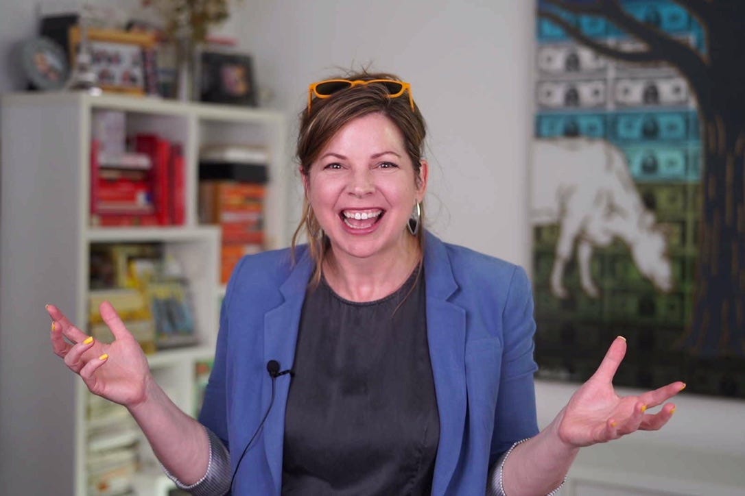 me smiling and making a broad gesture with a colorful bookshelf behind me