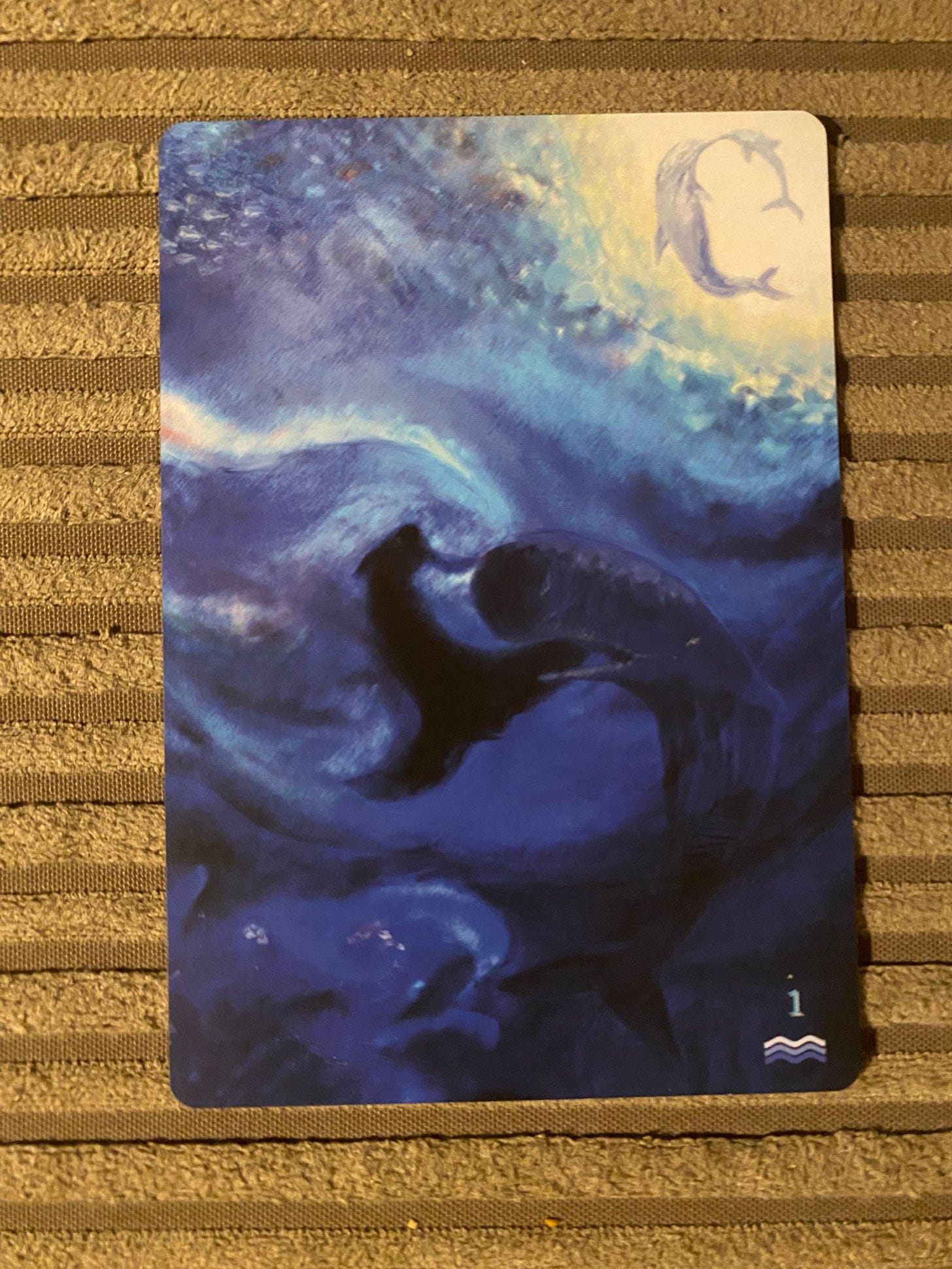 Water-themed card from the Shimmering Veil Tarot showing two whale-like forms circling through deep blue water beneath a pale moon, numbered 1 with wave symbol, used in the Tarot DMs interview with Alice Slater by Finbarre Snarey.
