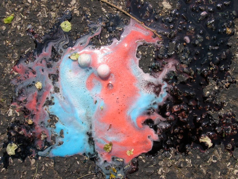 superman ice cream melts on the  cement in an oozing red and baby-blue color on a sunny day.