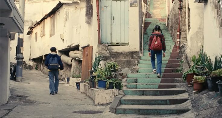 This may contain: two people are walking up the stairs in an alleyway with potted plants on either side