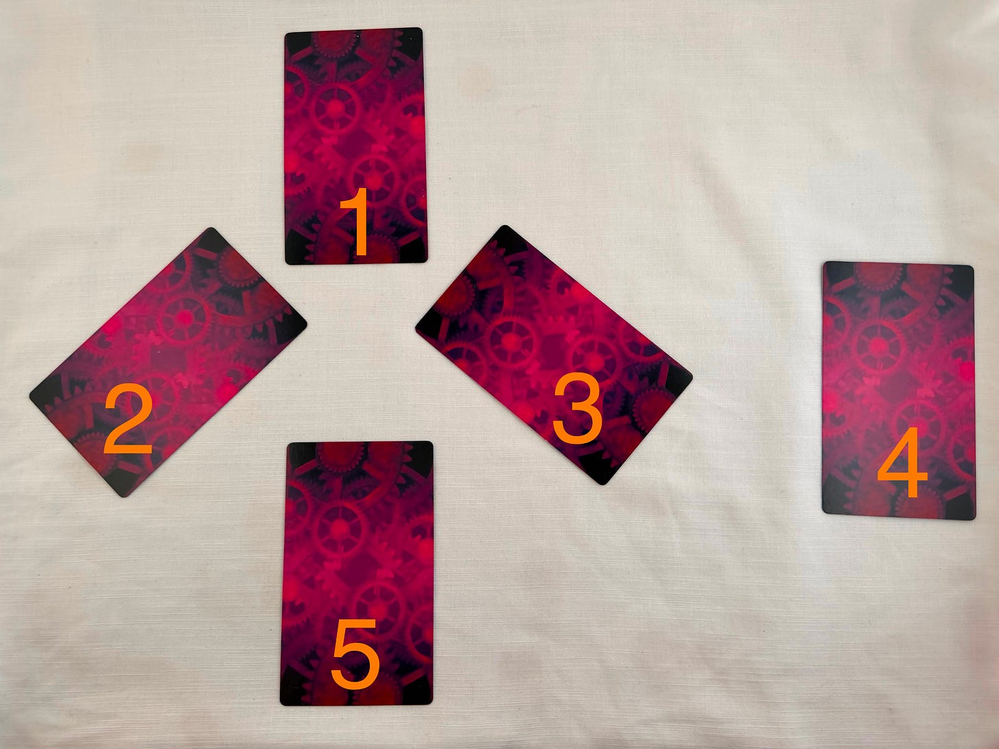 Five face-down tarot cards from the Choose Your Own Adventure Tarot Deck arranged in a branching path layout on a white linen backdrop. The cards have a deep red and purple gear-pattern back design. Card 1 sits at the top center. Cards 2 and 3 fan out below it like a fork in the road, with Card 2 angled to the left and Card 3 angled to the right. Card 4 sits off to the far right — the path almost not taken. Card 5 sits at the bottom center, where all the paths eventually meet. Each card is labeled with its number in orange text. Five face-down tarot cards from the Choose Your Own Adventure Tarot Deck arranged in a branching path layout on a white linen backdrop. The cards have a deep red and purple gear-pattern back design. Card 1 sits at the top center. Cards 2 and 3 fan out below it like a fork in the road, with Card 2 angled to the left and Card 3 angled to the right. Card 4 sits off to the far right — the path almost not taken. Card 5 sits at the bottom center, where all the paths eventually meet. Each card is labeled with its number in orange text.