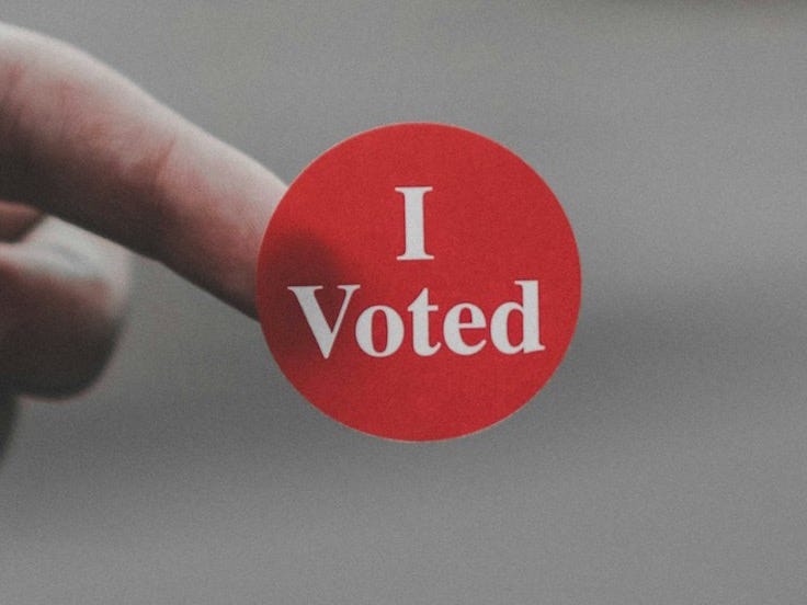 a hand holding a red button that says i vote a hand holding a red button that says i vote