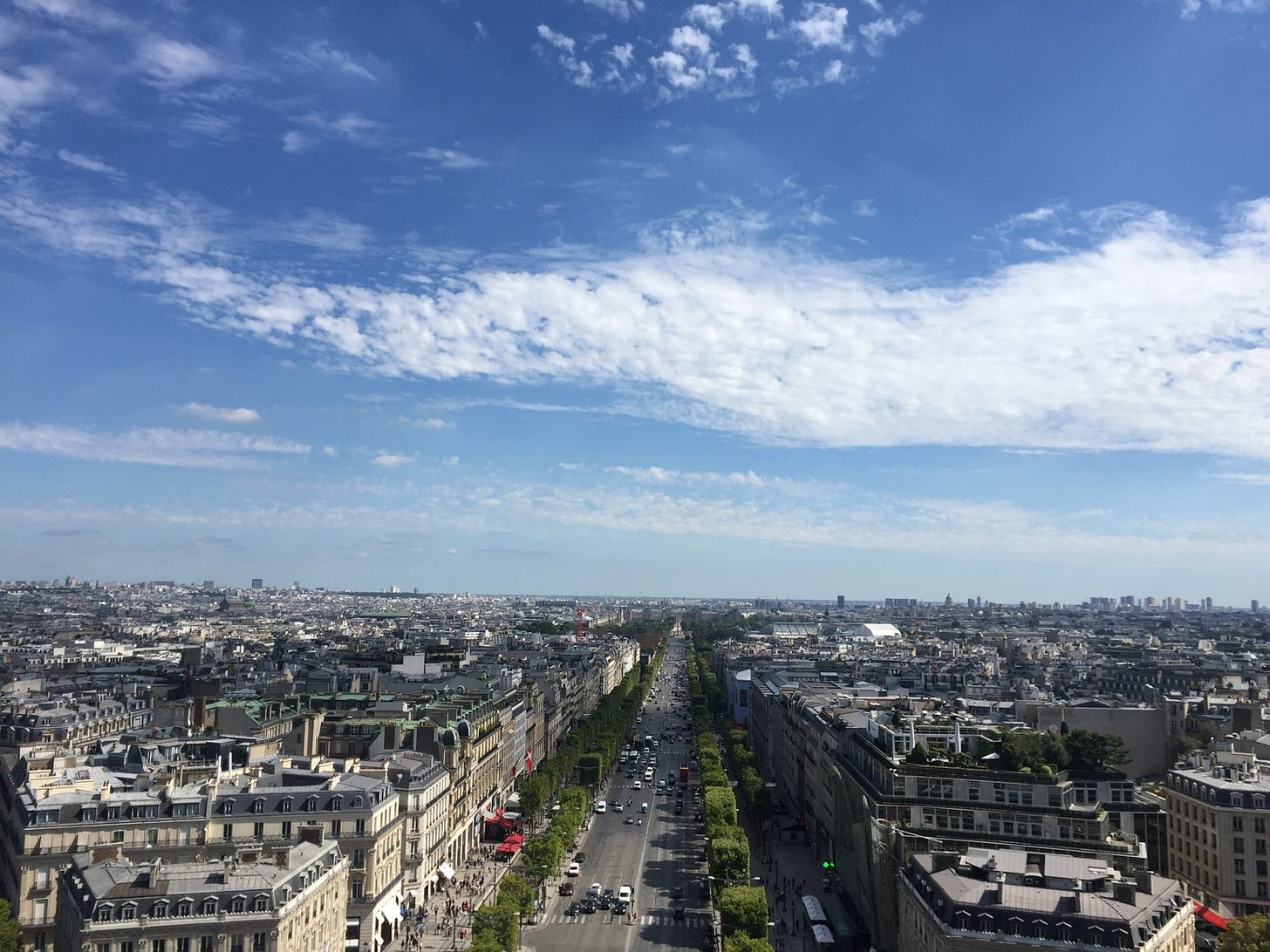The broad Champs-Élysées stretches through Paris, where rows of mature platanes (plane trees) frame the avenue and create a sense of enclosure despite its immense scale.