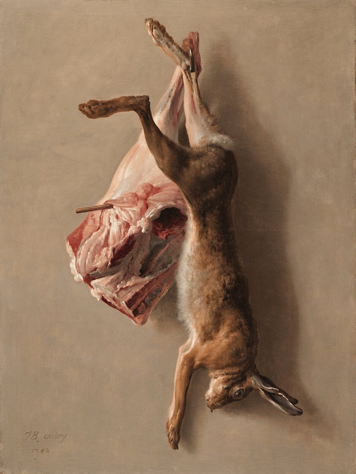 Oil painting by Jean-Baptiste Oudry featuring a whole, furred hare and a butchered leg of lamb hanging from a dark hook against a neutral stone wall. To the right, the tawny hare hangs vertically, its head downward with a glassy eye and a small drop of blood at the snout. To the left, the raw lamb shows translucent pinks, deep reds, and marbled white fat. Soft, directional light emphasizes the contrast between the tactile fur and the slick, exposed meat. Part of the In the Flesh series at The Subtext Review.
