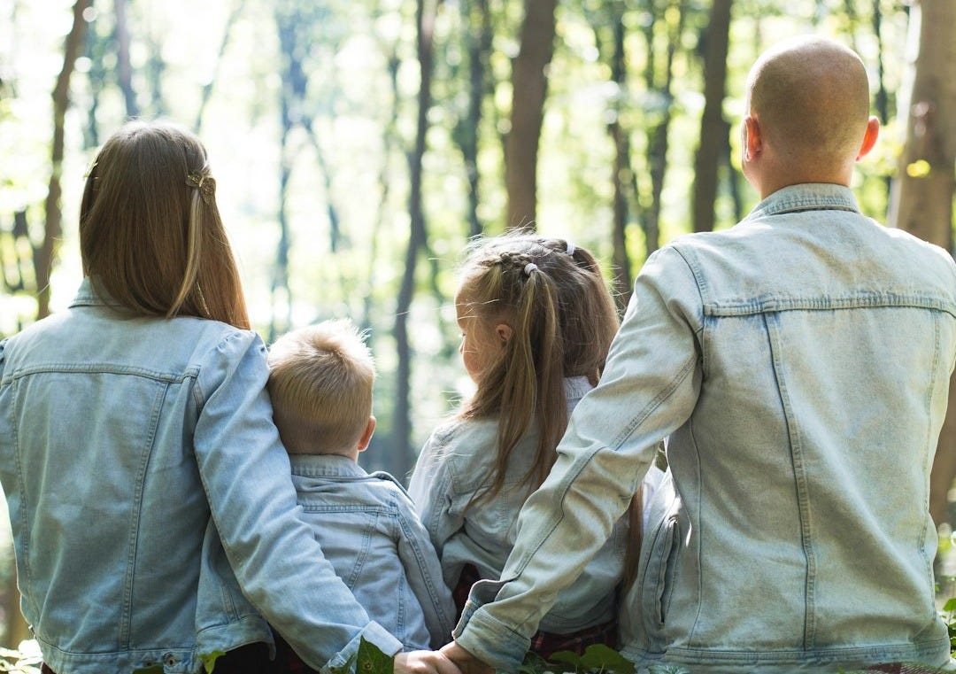 man and woman holding hands together with boy and girl looking at green trees during day