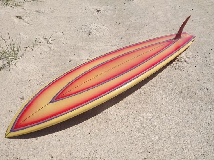 This may contain: a red and yellow surfboard laying in the sand