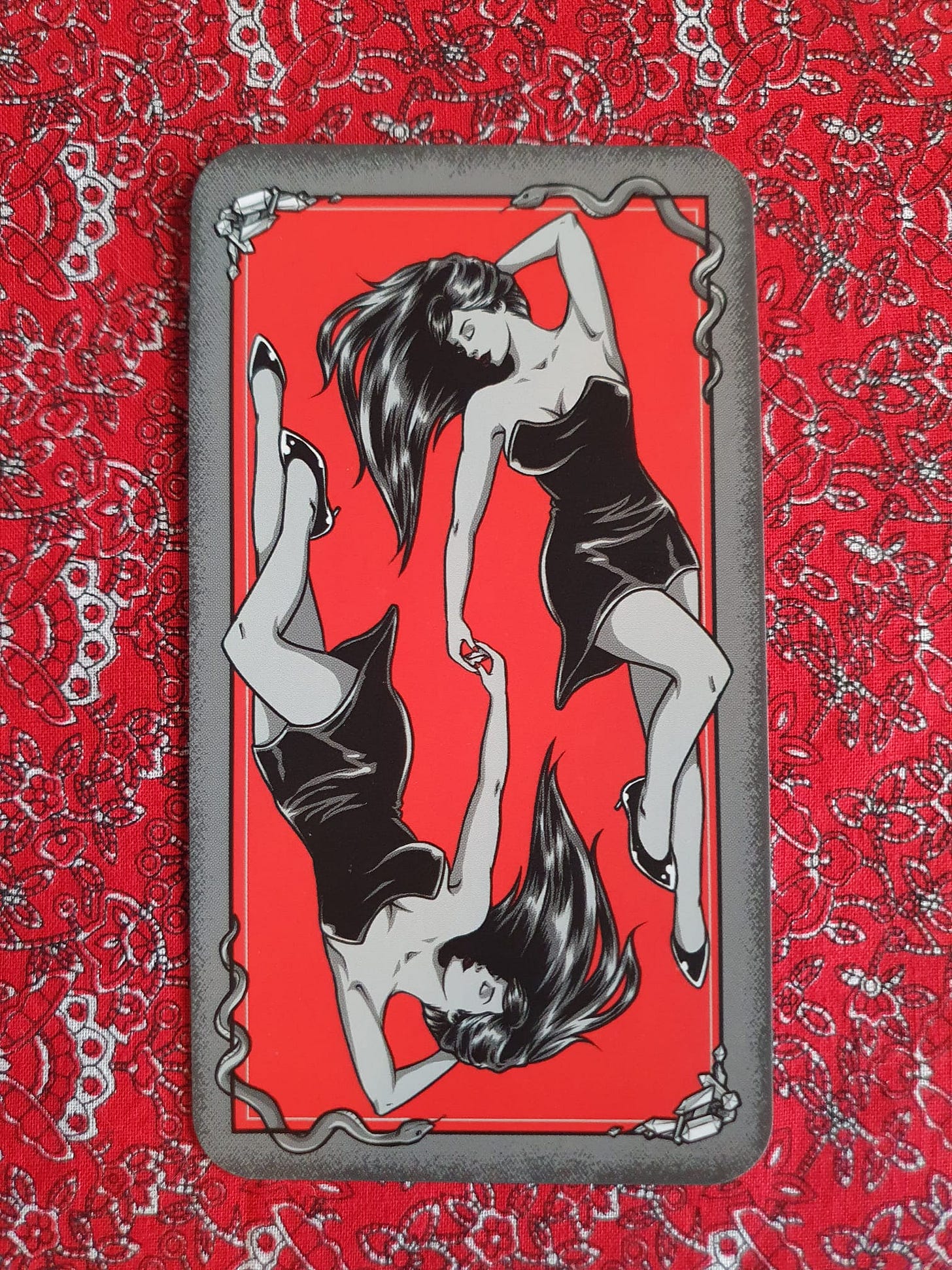 Card from Michelle Lodge’s Bad Witch Tarot showing two women in black dresses holding hands against a red background, framed by snakes and crystals. Card from Michelle Lodge’s Bad Witch Tarot showing two women in black dresses holding hands against a red background, framed by snakes and crystals.