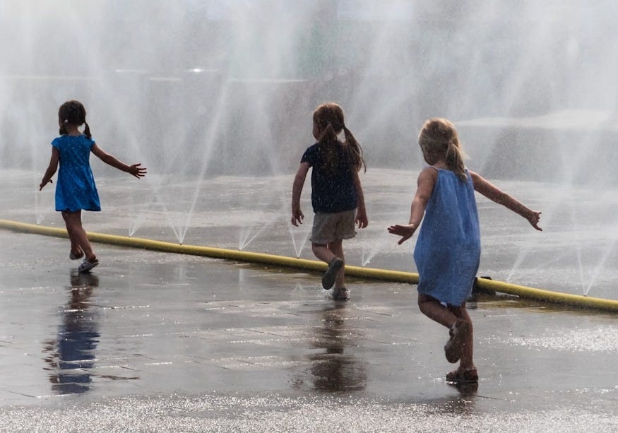 three girls running beside water fountains