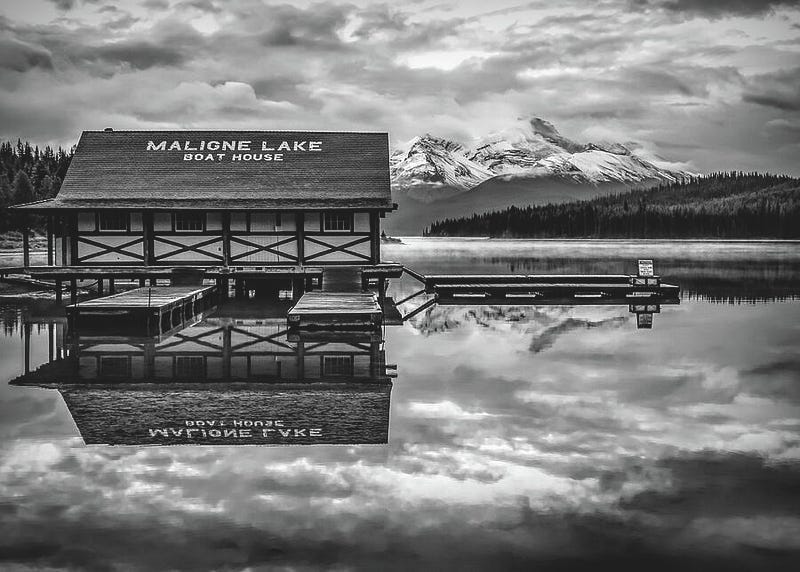 A calm black and white scene of Maligne Lake in the Canadian Rockies, with still water reflecting mountains and sky in perfect symmetry.