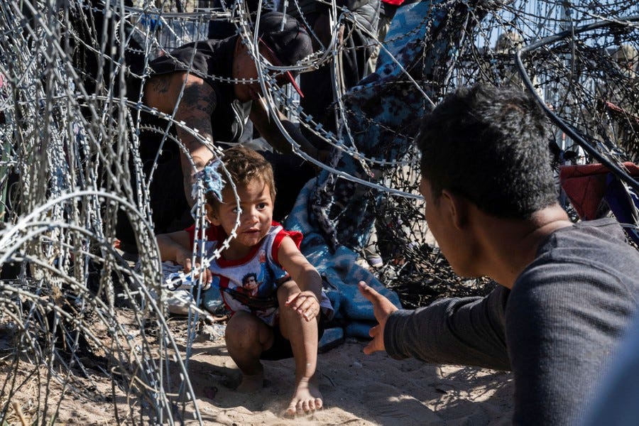 A young boy is helped as he crawls through a concertina wire barrier at the U.S.-Mexico border.