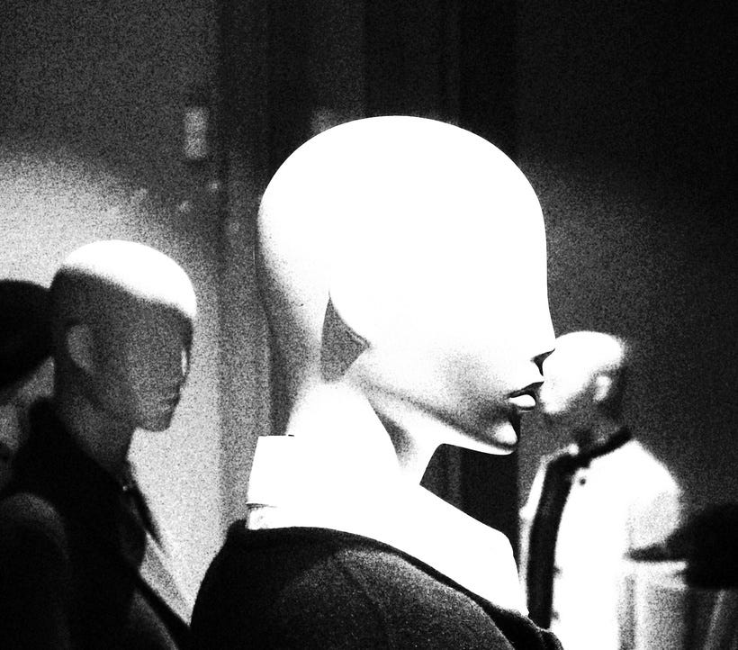 A grainy black and white picture of three mannequins, all facing different directions, with one strongly foregrounded. All three are bald, and the blown-out contrast makes it impossible to see their features beyond the strong lip and jawline of the closest one. They are wearing shirts or jackets with strong collars. A grainy black and white picture of three mannequins, all facing different directions, with one strongly foregrounded. All three are bald, and the blown-out contrast makes it impossible to see their features beyond the strong lip and jawline of the closest one. They are wearing shirts or jackets with strong collars.