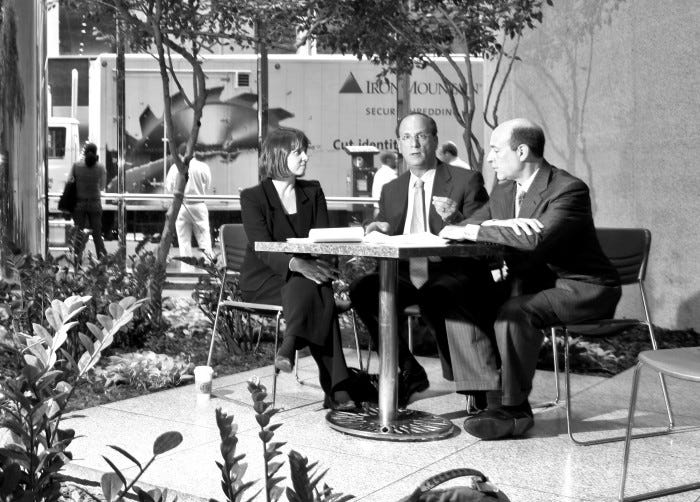 Three business executives – BlackRock’s Susan Wagner, Larry Fink and Robert Kapito – sitting at table outside in the sunshine in New York