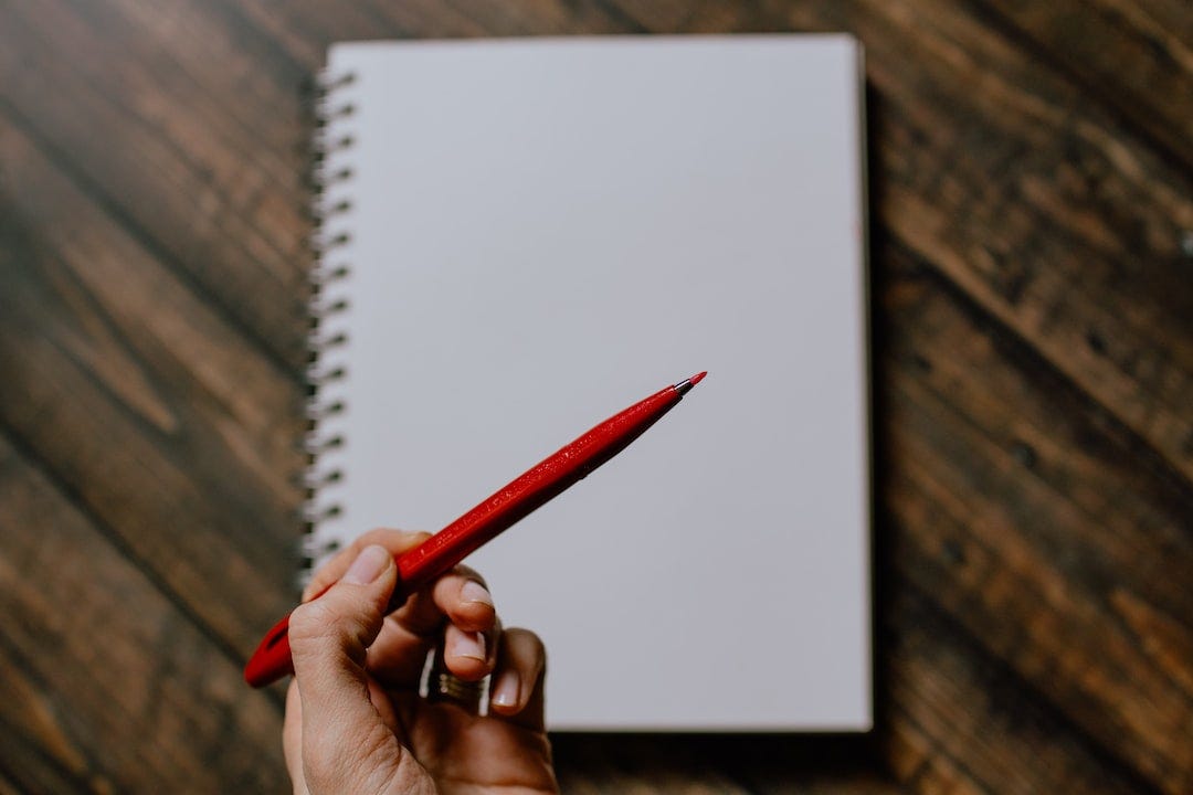 person holding red pencil writing on white paper person holding red pencil writing on white paper