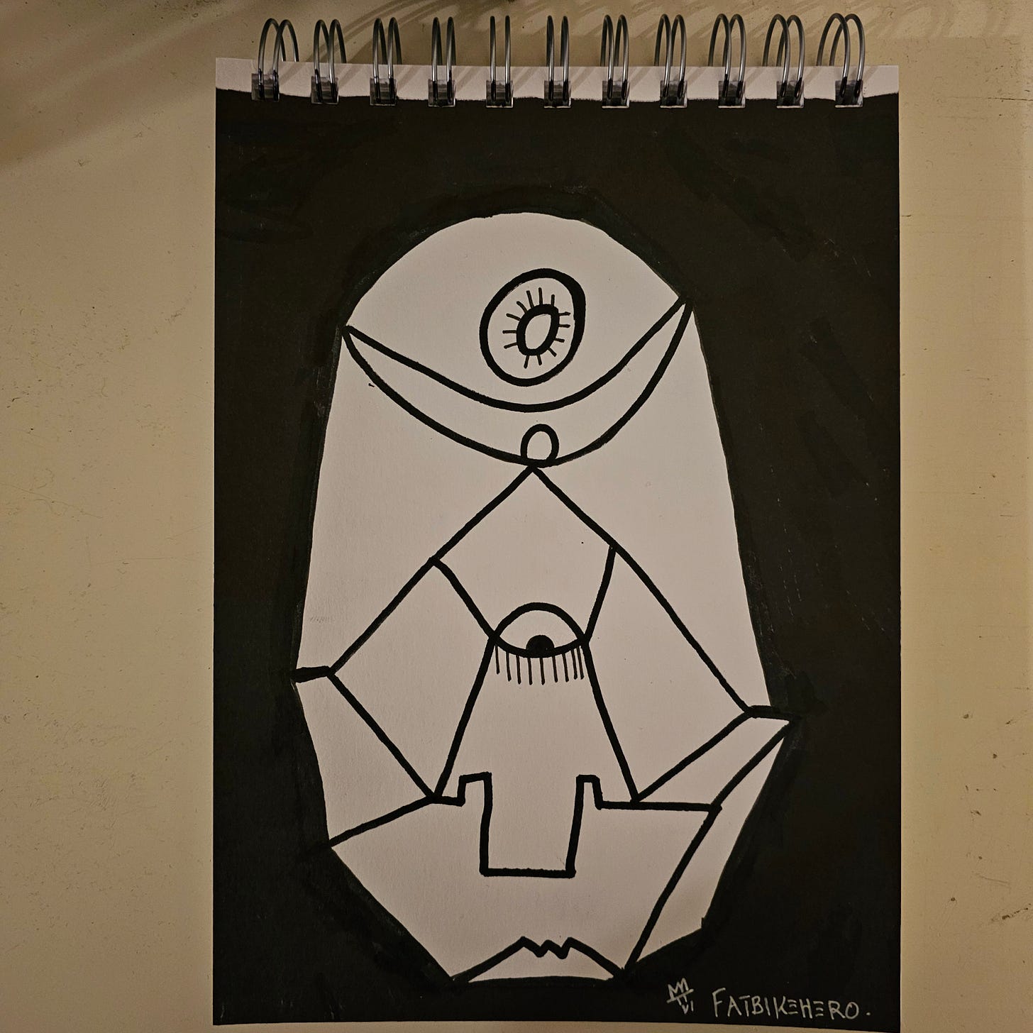 A high-contrast black and white ink drawing of a geometric, totem-like face or shield. It features a central eye with lashes, a superior "third eye" or sun motif within a crescent, and segmented, angular lines forming a jaw or base. The style is graphic and neo-tribal.