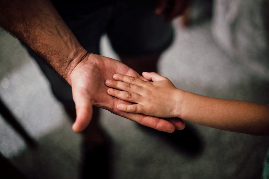 Free Close-up of a child's hand resting gently on a man's hand, symbolizing love and support. Stock Photo