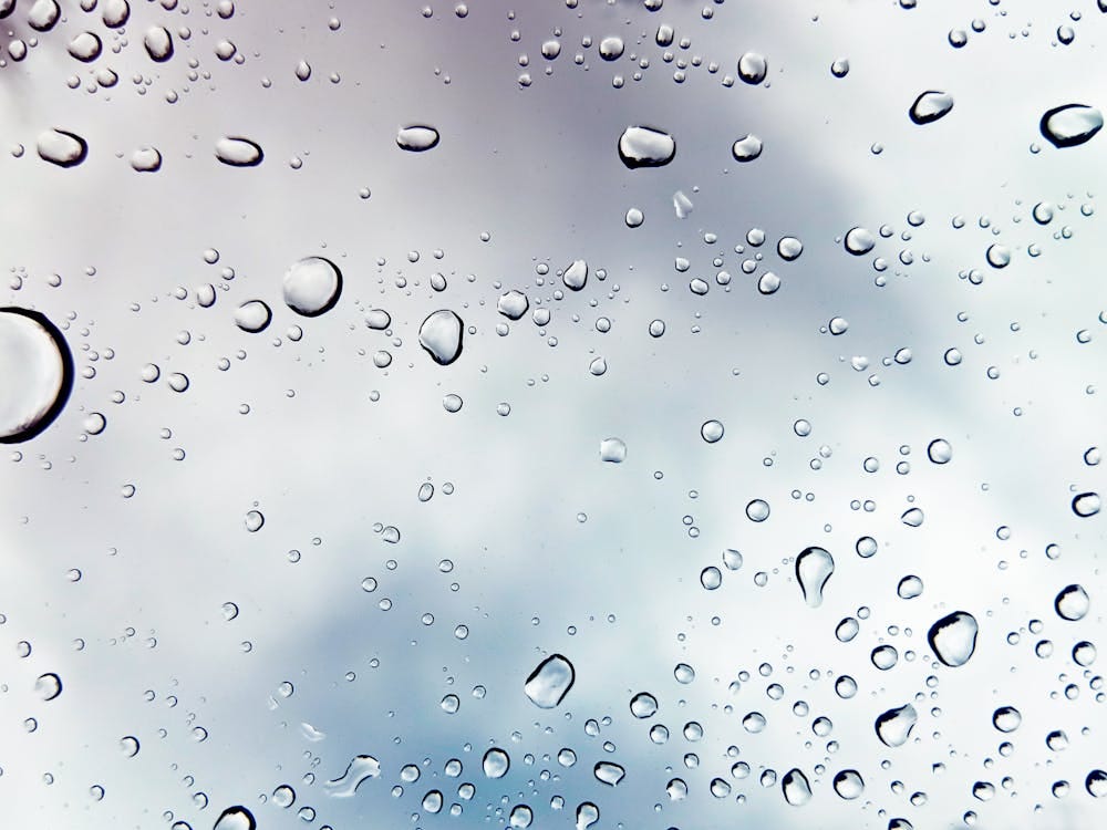 Free Raindrops on a window against a cloudy sky, creating a peaceful mood. Stock Photo