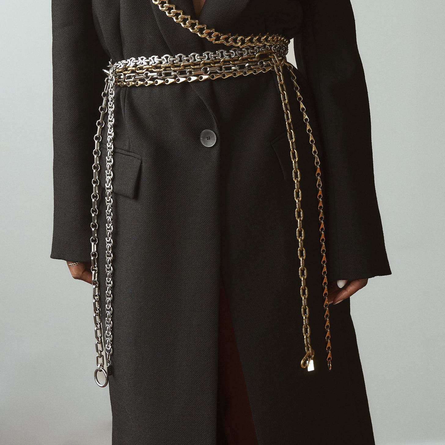 Front view of a black wool coat featuring the Lapo Lounge Eris, Hyperion, Himalia, and Zira link belts and a crossbody gold chain.
