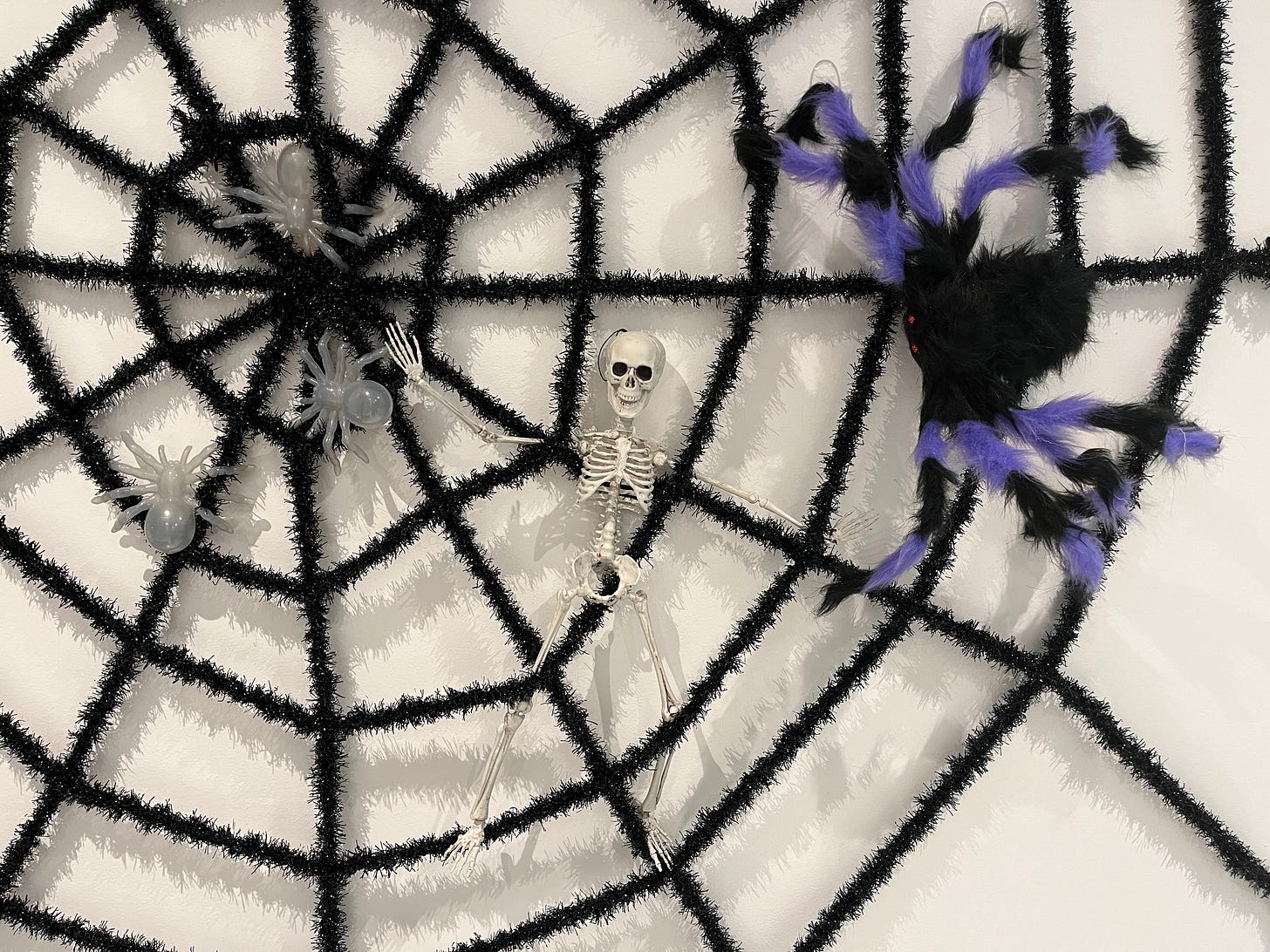 A photograph of a toy skeleton trapped in a large fake black spiderweb with a large purple and black toy spider appearing as if it is crawling toward him.
