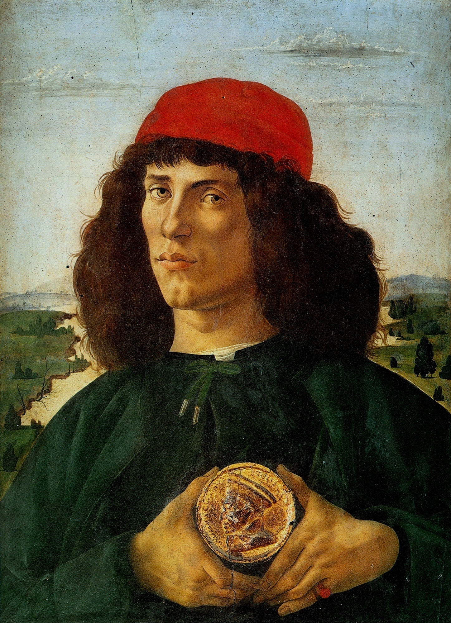 A young man with curly hair, seen to the chest against a landscape, holding up a round gilded medal with a profile portrait between his fingers.