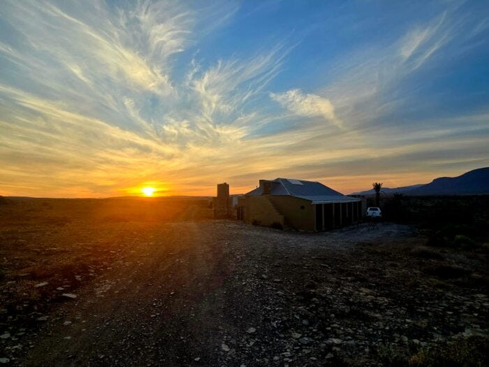 Desert farmhouse silhouette at golden sunset with dramatic wispy clouds and gravel road Desert farmhouse silhouette at golden sunset with dramatic wispy clouds and gravel road
