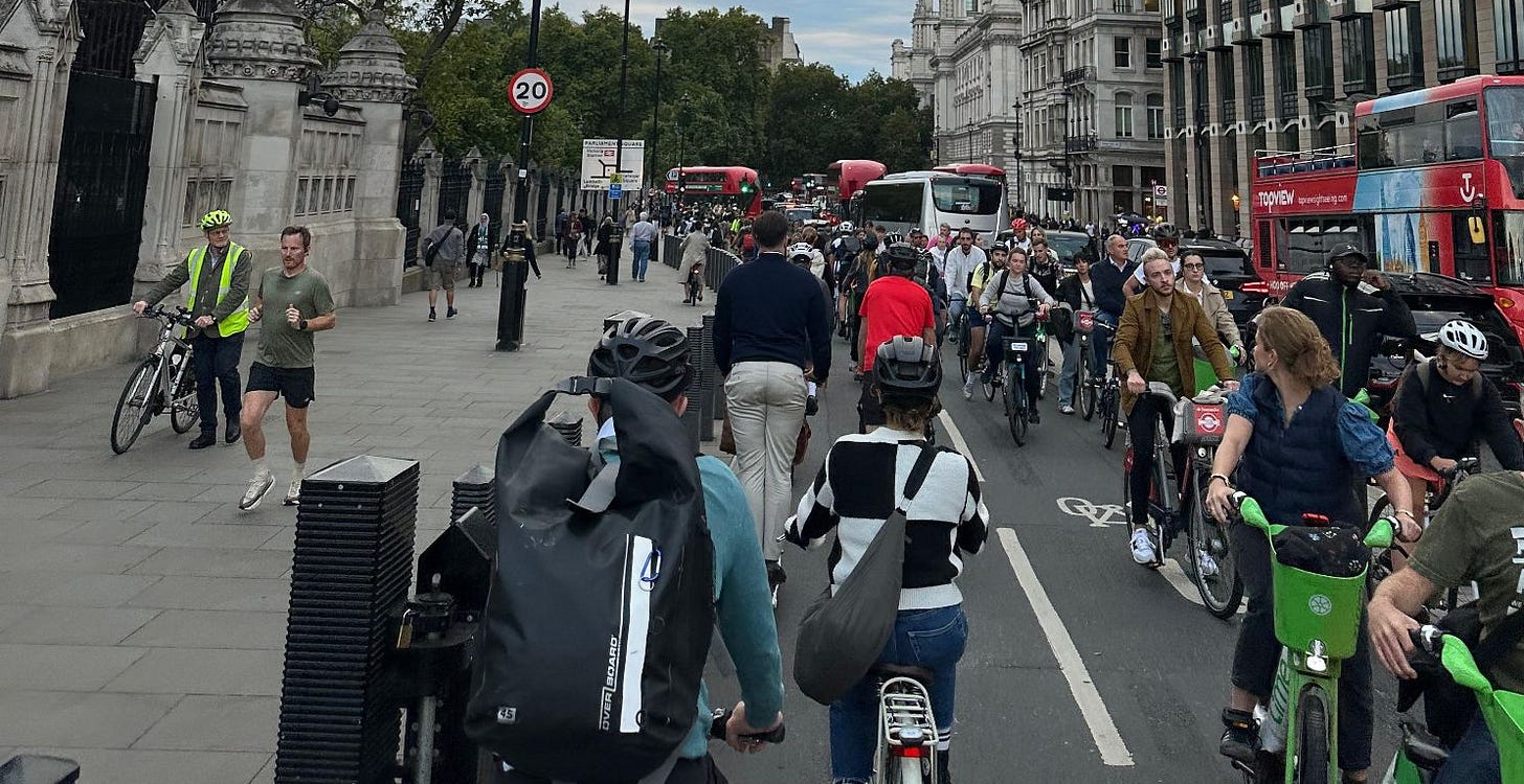 A long queue of cyclists from the foreground to traffic lights 100m away in the distance. There is a queue of cyclists in the opposite direction too.