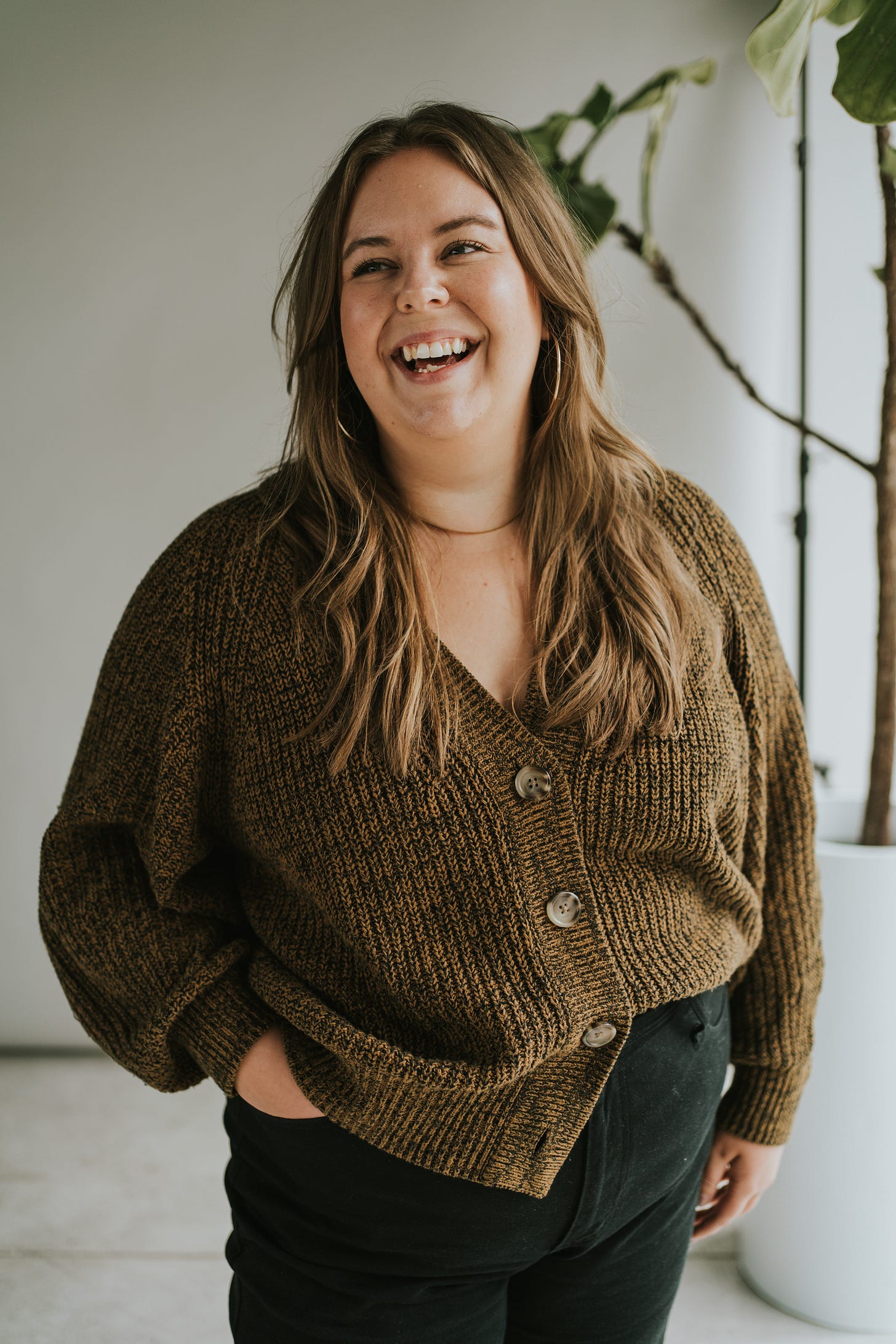Melissa wearing a brown buttoned cardigan, looking off to the side & laughing