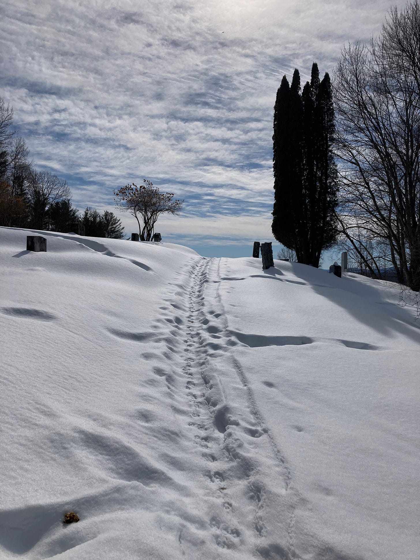 footprints in the snow heading uphill toward bright sun and whispy clouds footprints in the snow heading uphill toward bright sun and whispy clouds