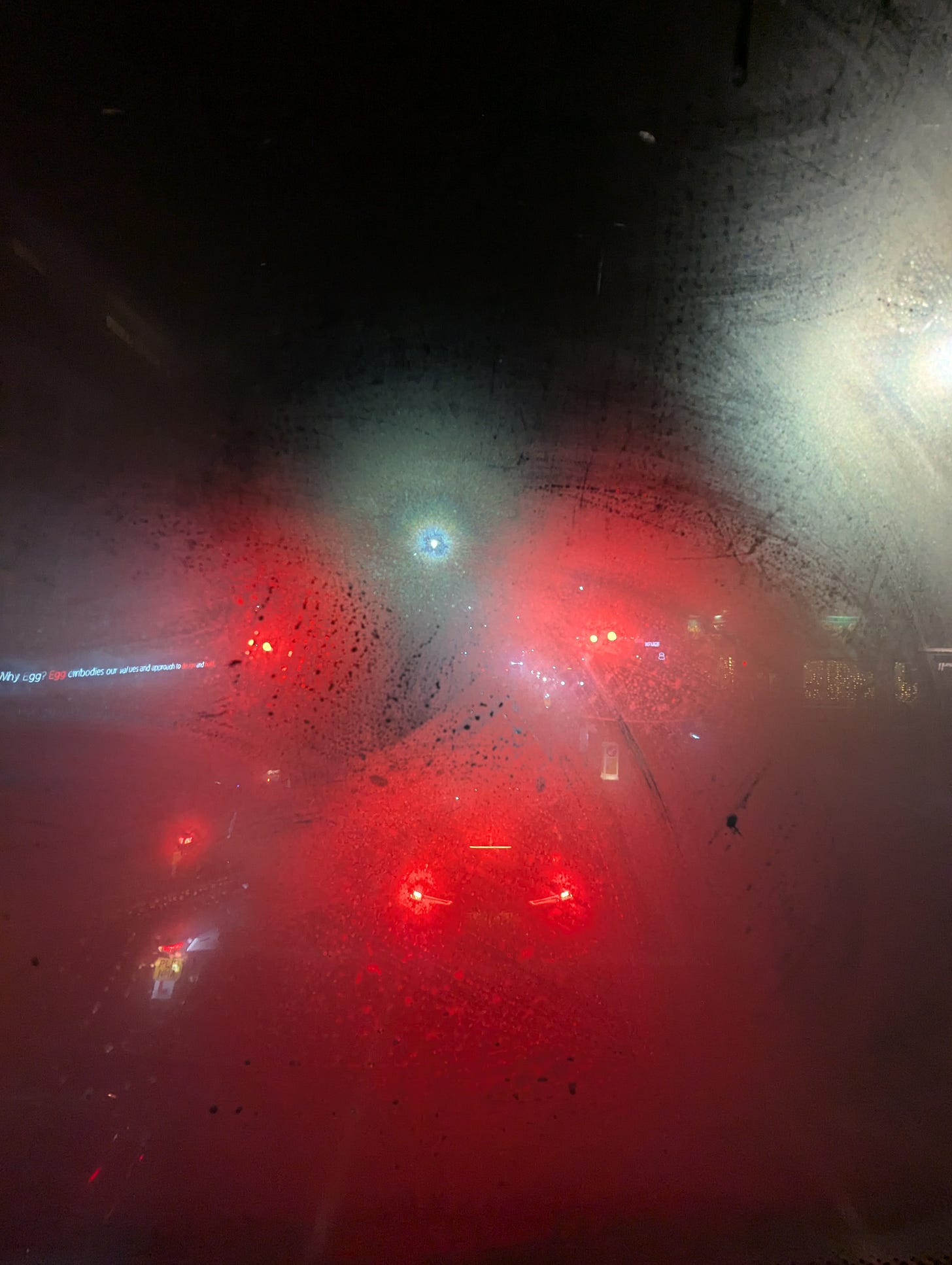 A fogged up bus window at night time, with traffic and car lights pouring in.
