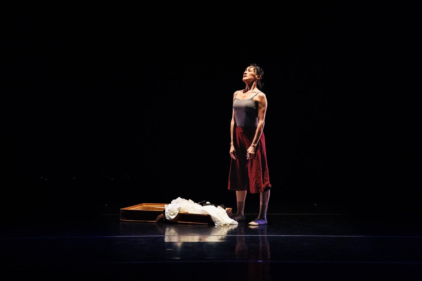 A person in a grey tank top and red skirt standing on a stage

Description automatically generated