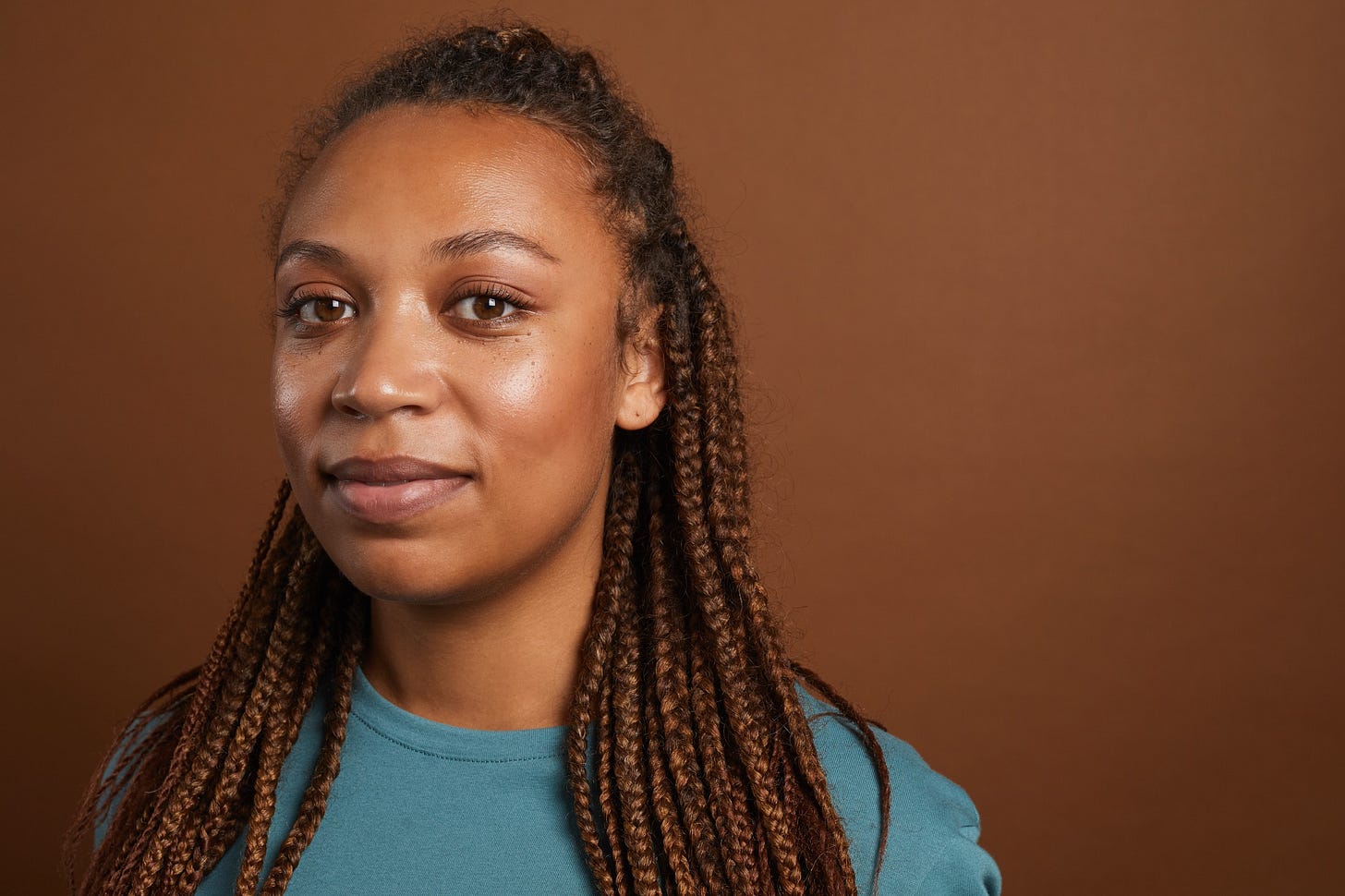 A beautiful Black woman with long braids smiles at the camera against a brown background. A beautiful Black woman with long braids smiles at the camera against a brown background.