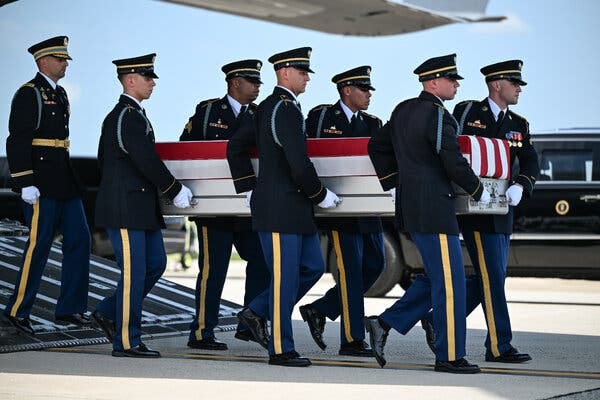 Six soldiers carry a coffin with an American flag draped over it.