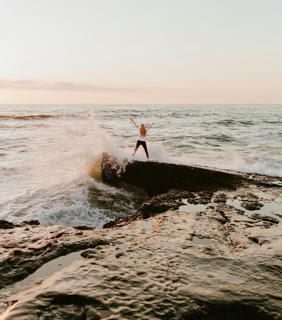 man in orange shirt standing on rock near sea during daytime