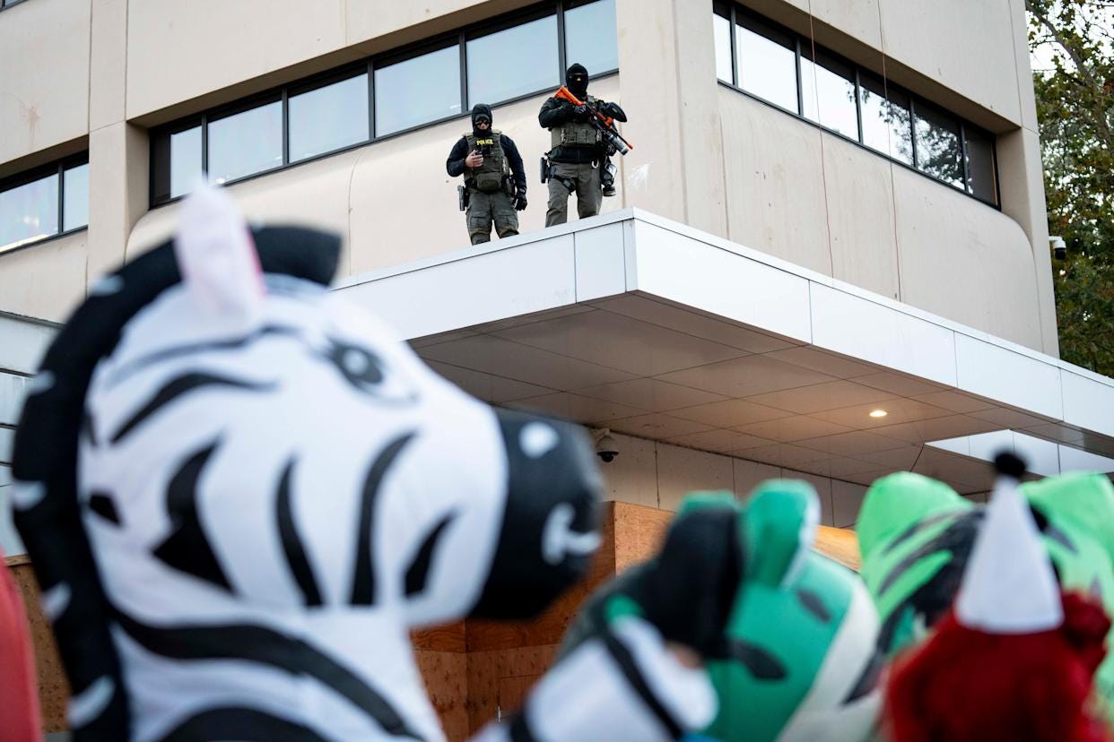 Federal officers watch protesters dressed in inflatable animal suits outside of the U.S. Immigration and Customs Enforcement facility in South Portland on Oct. 13, 2025.