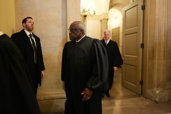 Associate Justice Clarence Thomas in a corridor of the Supreme Court building. He is wearing a black judicial robe. 