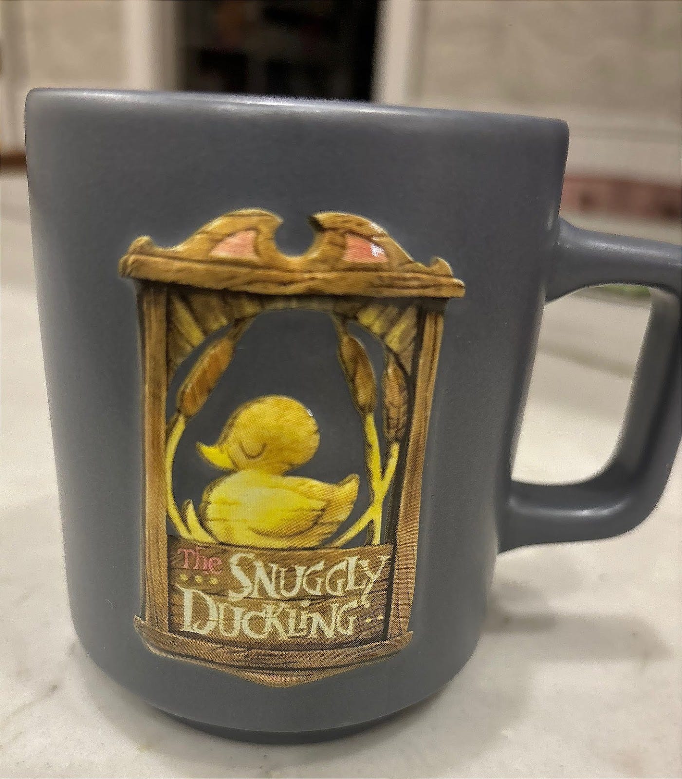 A mug that says Snuggly Duckling and has a cute yellow duckling on it