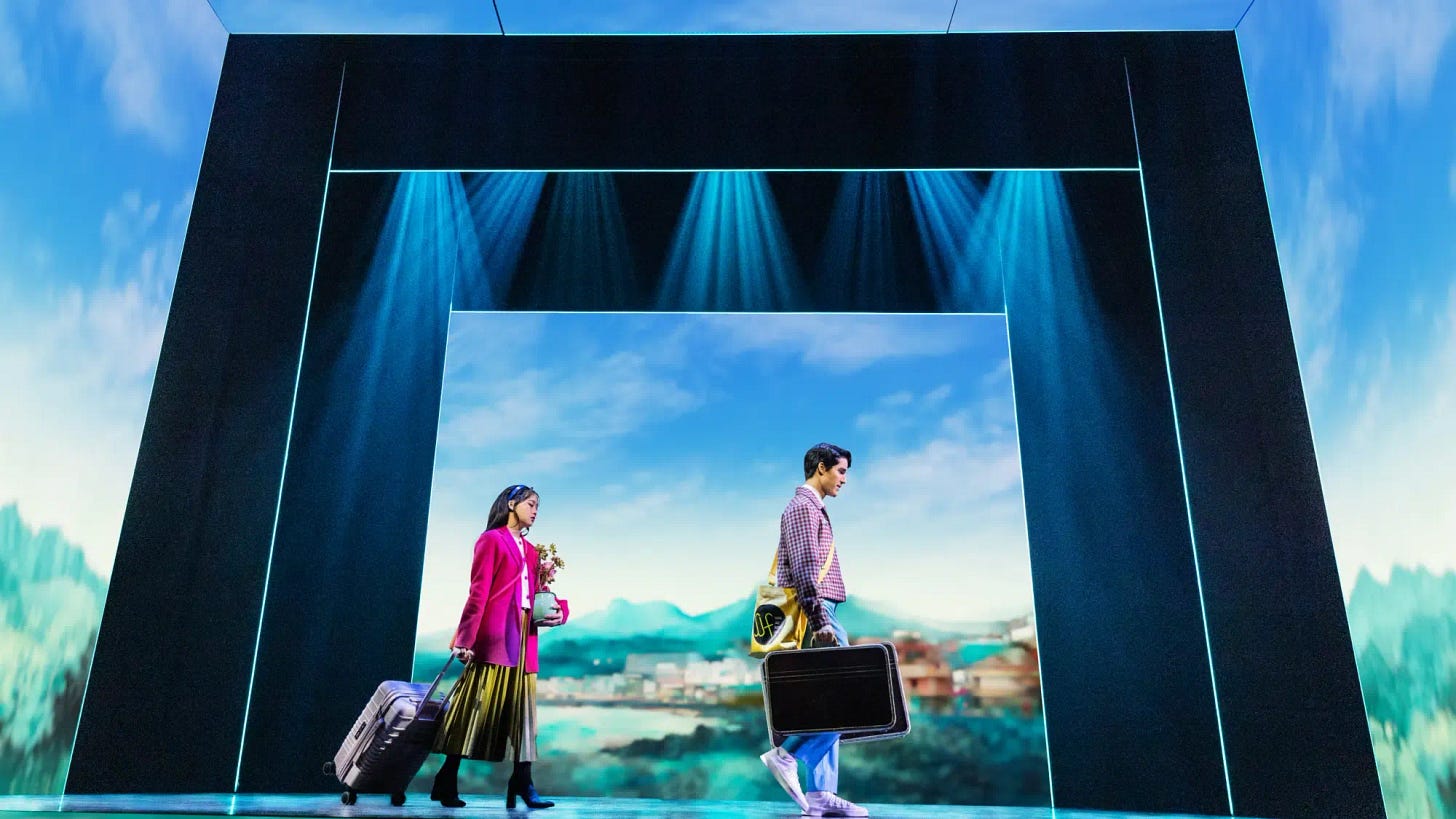 Helen J Shen and Darren Criss in character in 'Maybe Happy Ending,' carrying suitcases and walking forlornly across the stage